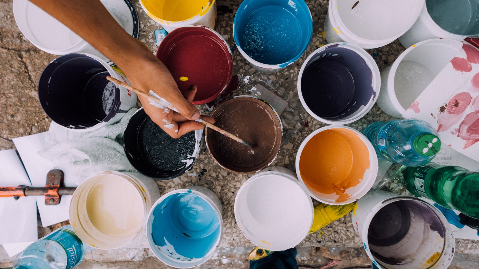 Buckets of different colors of paint with an artist dipping his or her paintbrush into one of the buckets