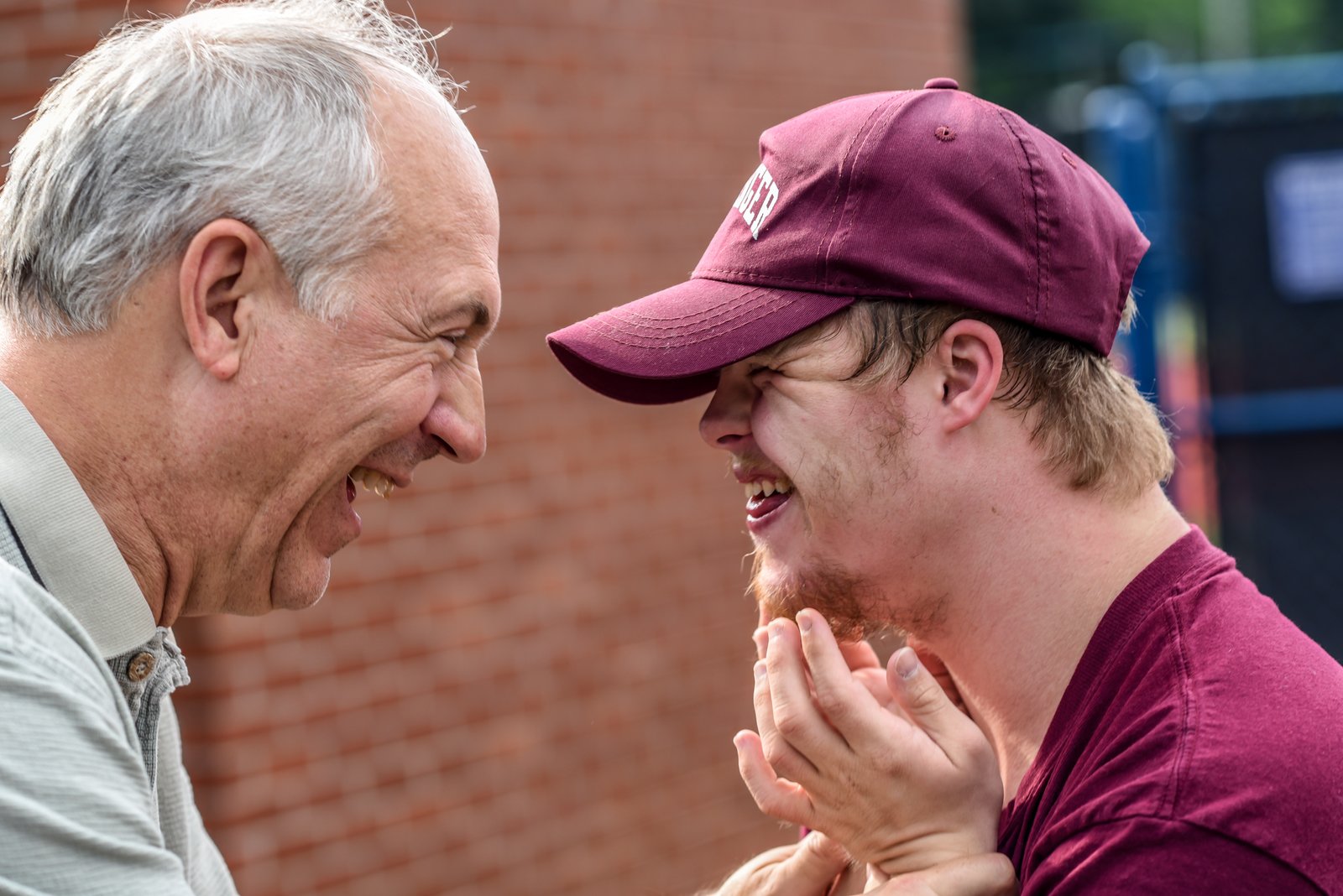 Older caucasian man smiling and laughing with young caucasian man who appears to have Down Syndrome
