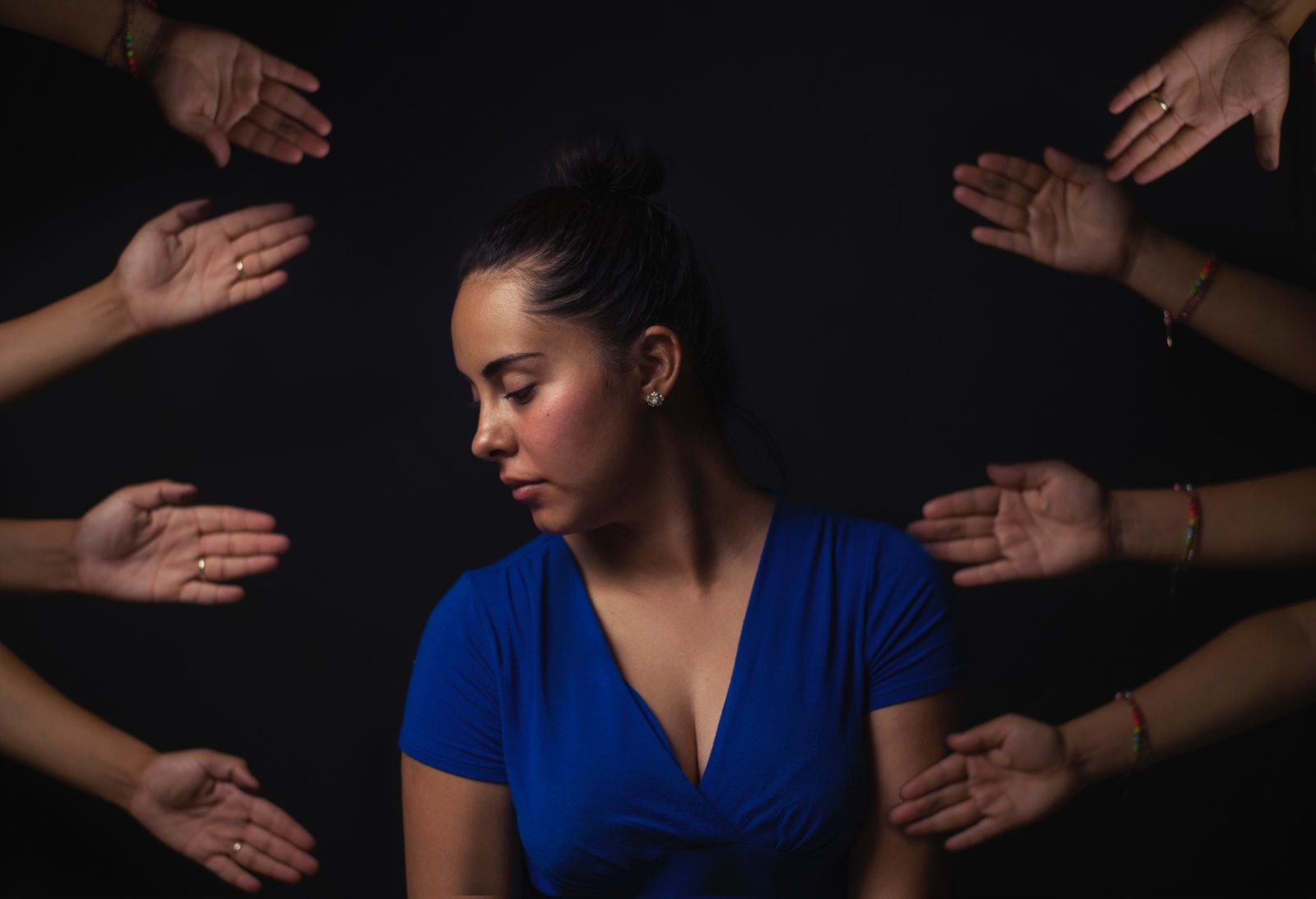 Young woman in blue, surrounded by hands reaching towards her from out of view