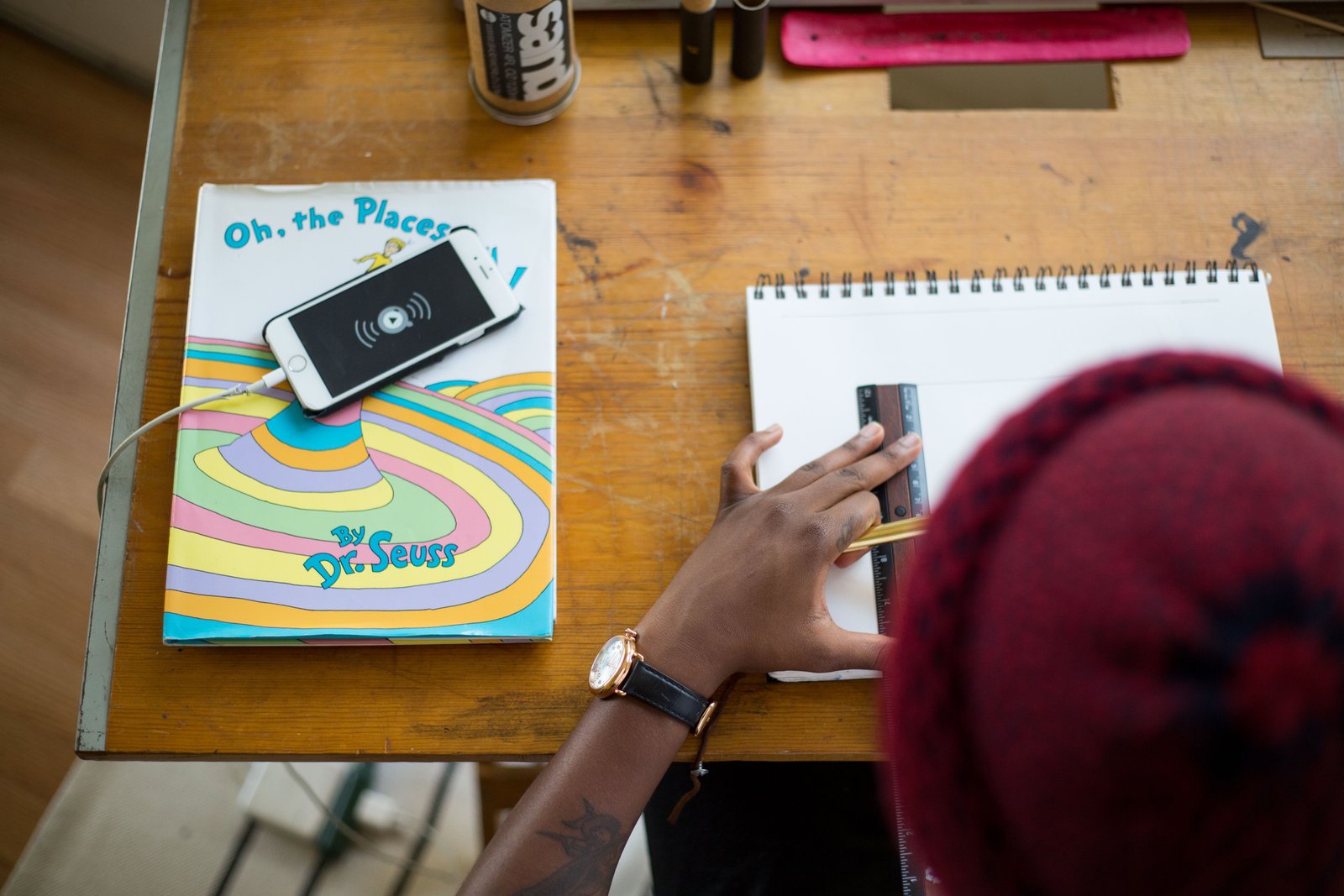 African American young adult using ruler to draw. Next to the notepad is "Oh, the Places You'll Go" by Dr. Seuss