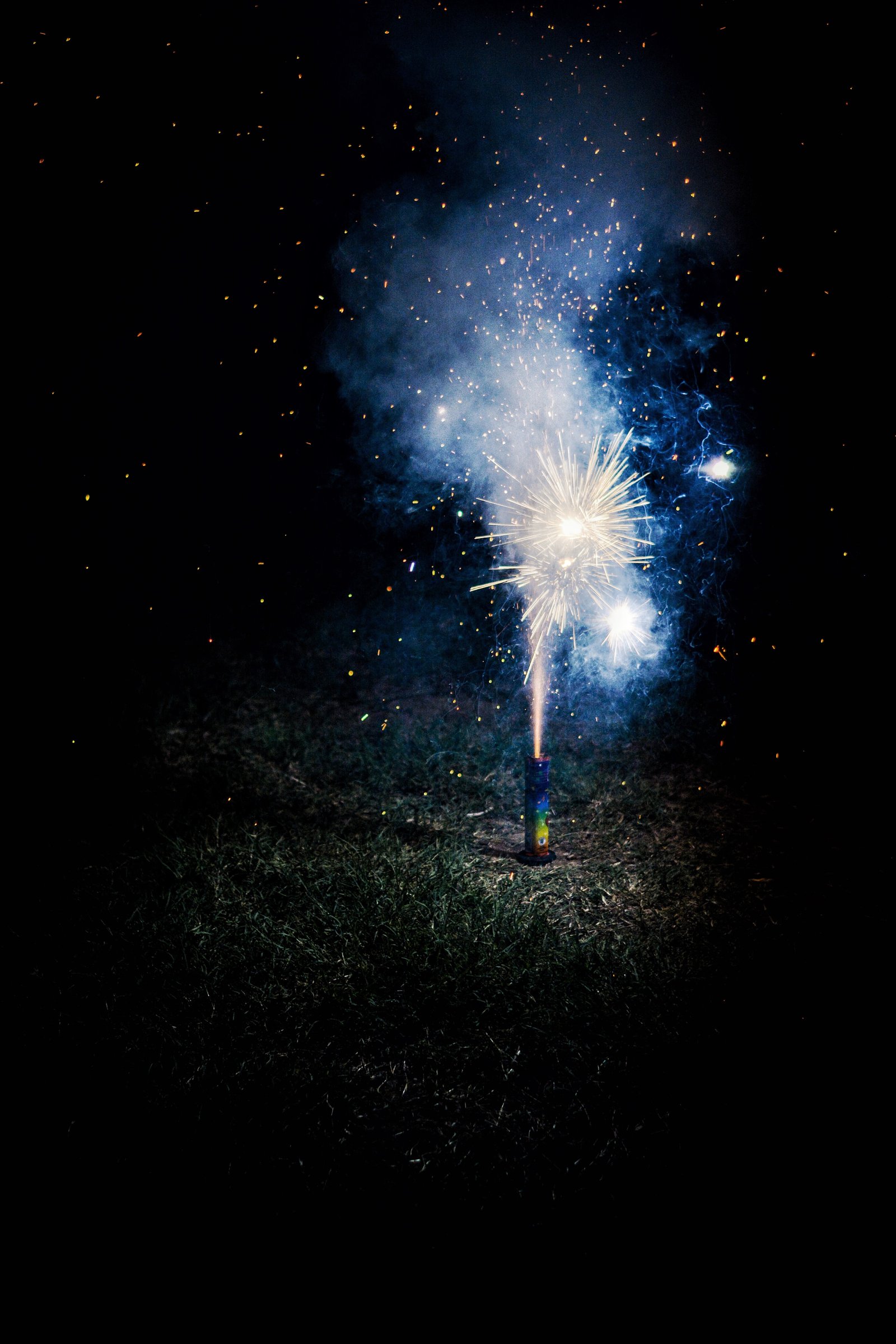 A firework candle on the ground, shooting sparks into the air with black background