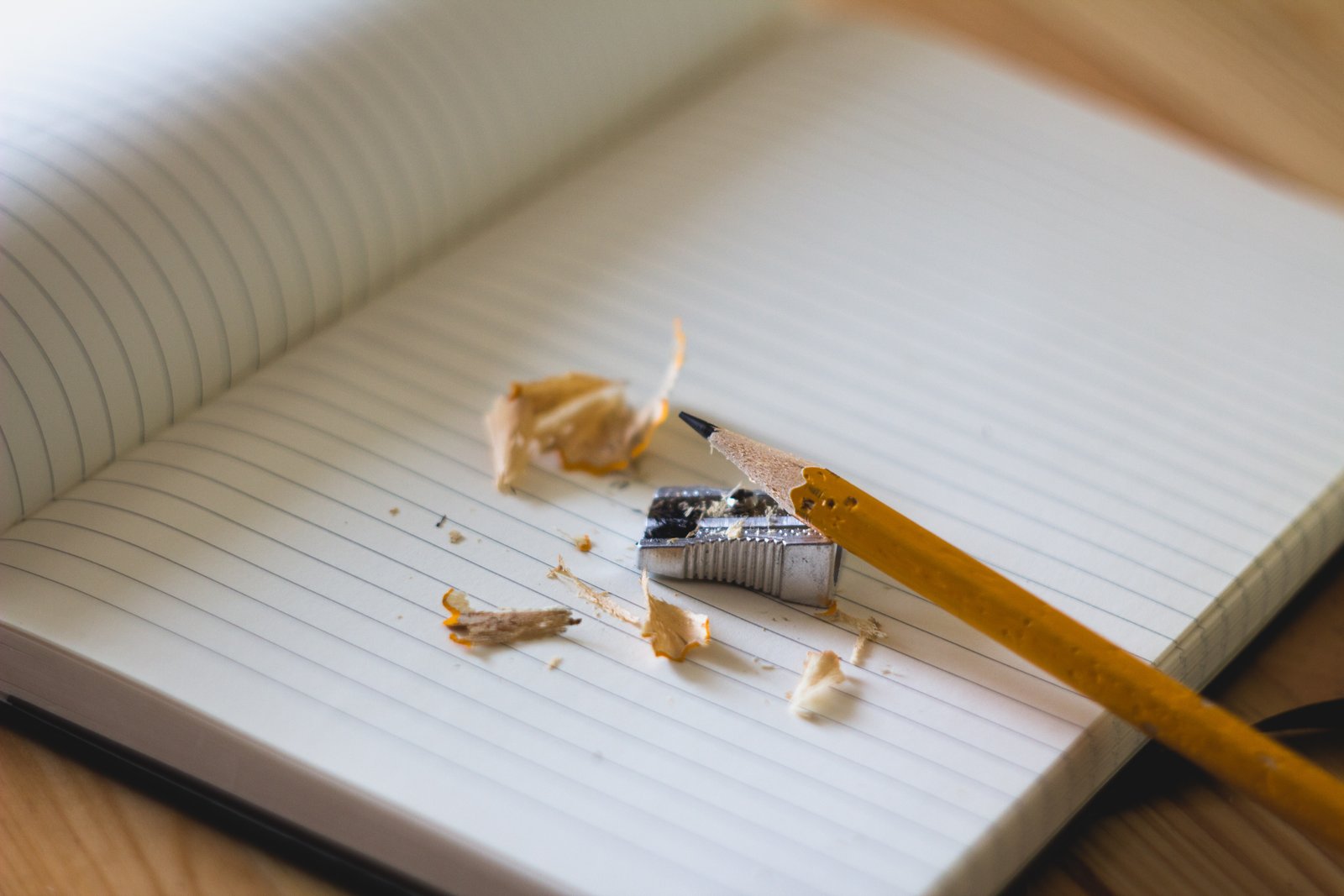 Image of a freshly sharpened pencil and a blank notebook. Pencil shavings are laying on the blank page.