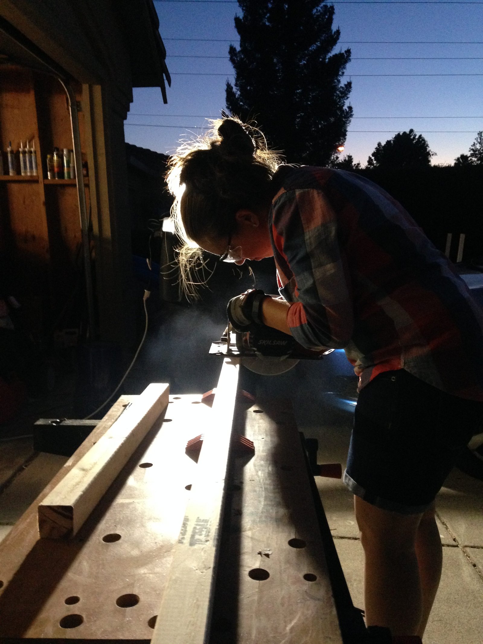 Young woman using circular saw with cool backlighting at night