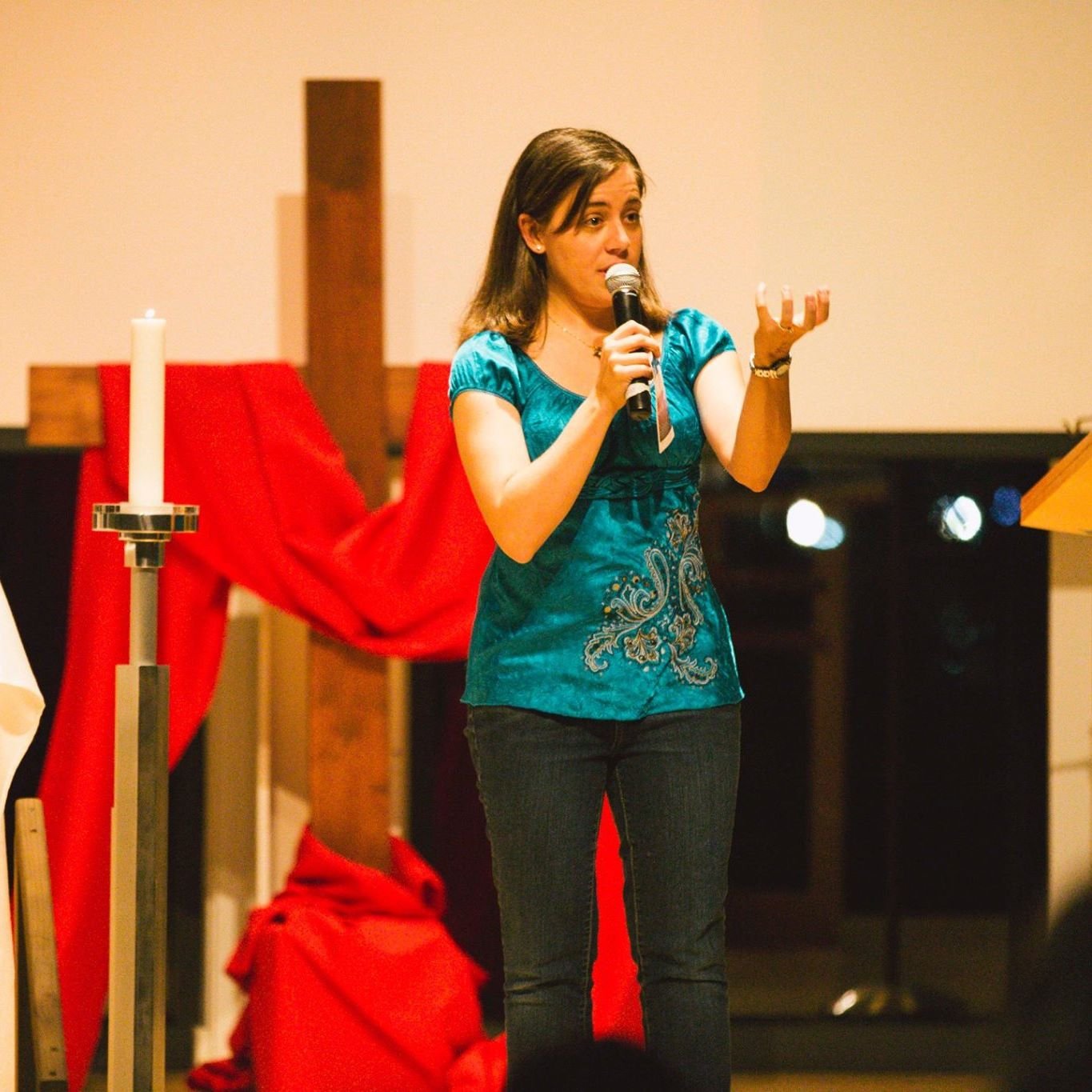Young woman speaking in microphone on stage, wearing turquoise top