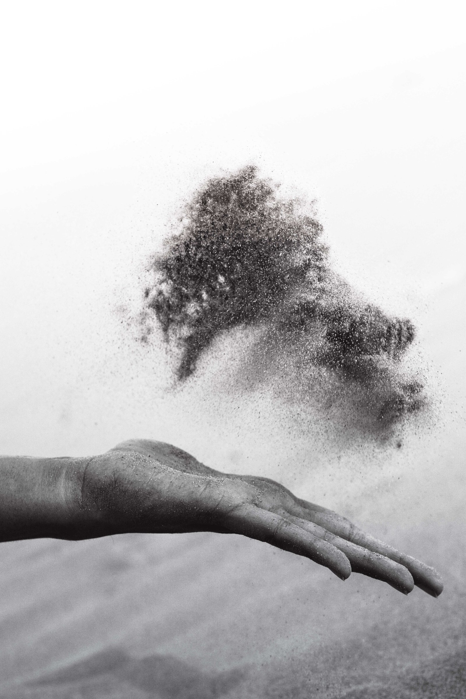 Black and white image of a dirty hand throwing a small cloud of ashes into the air