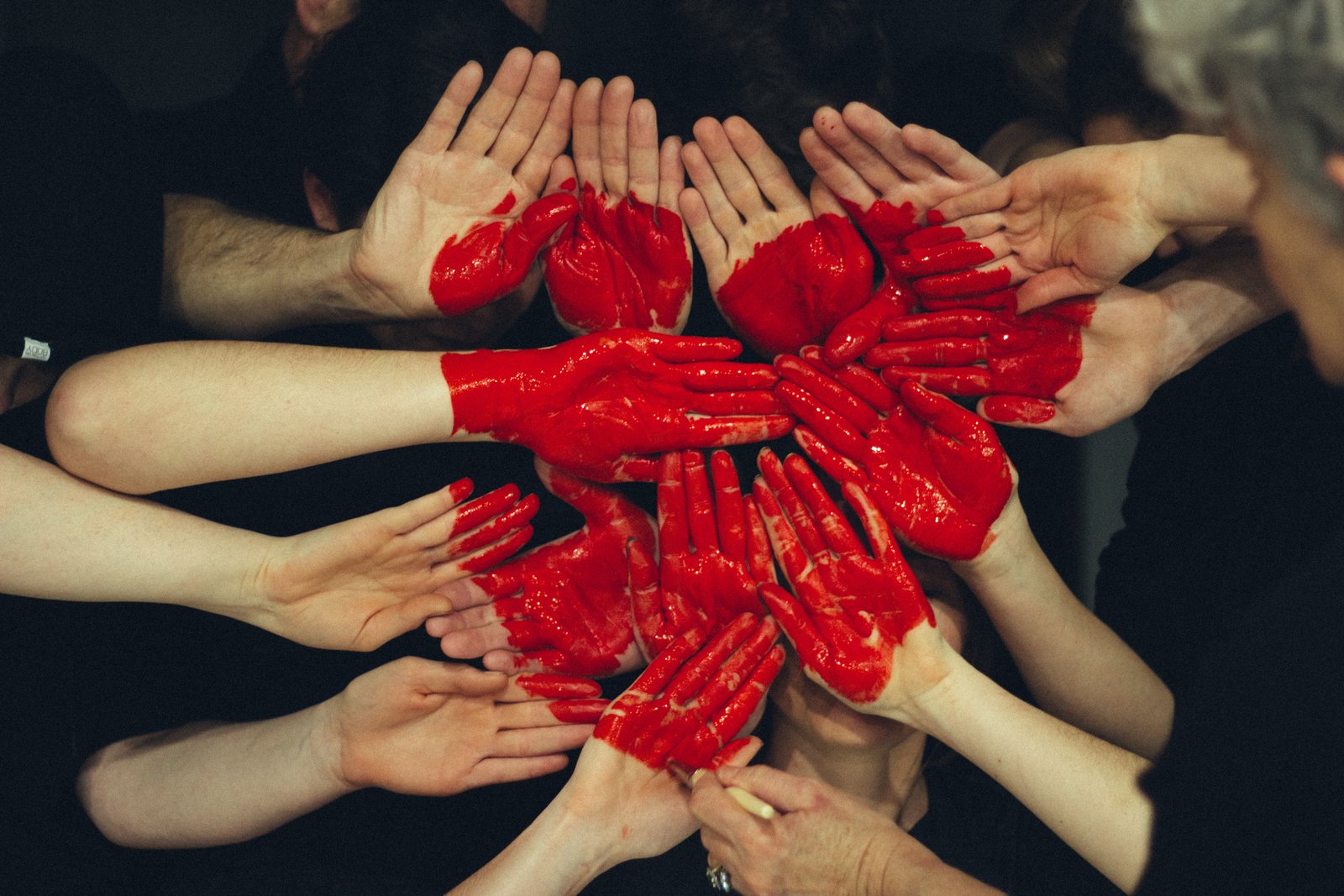 Multiple hands with red paint come together to form a heart