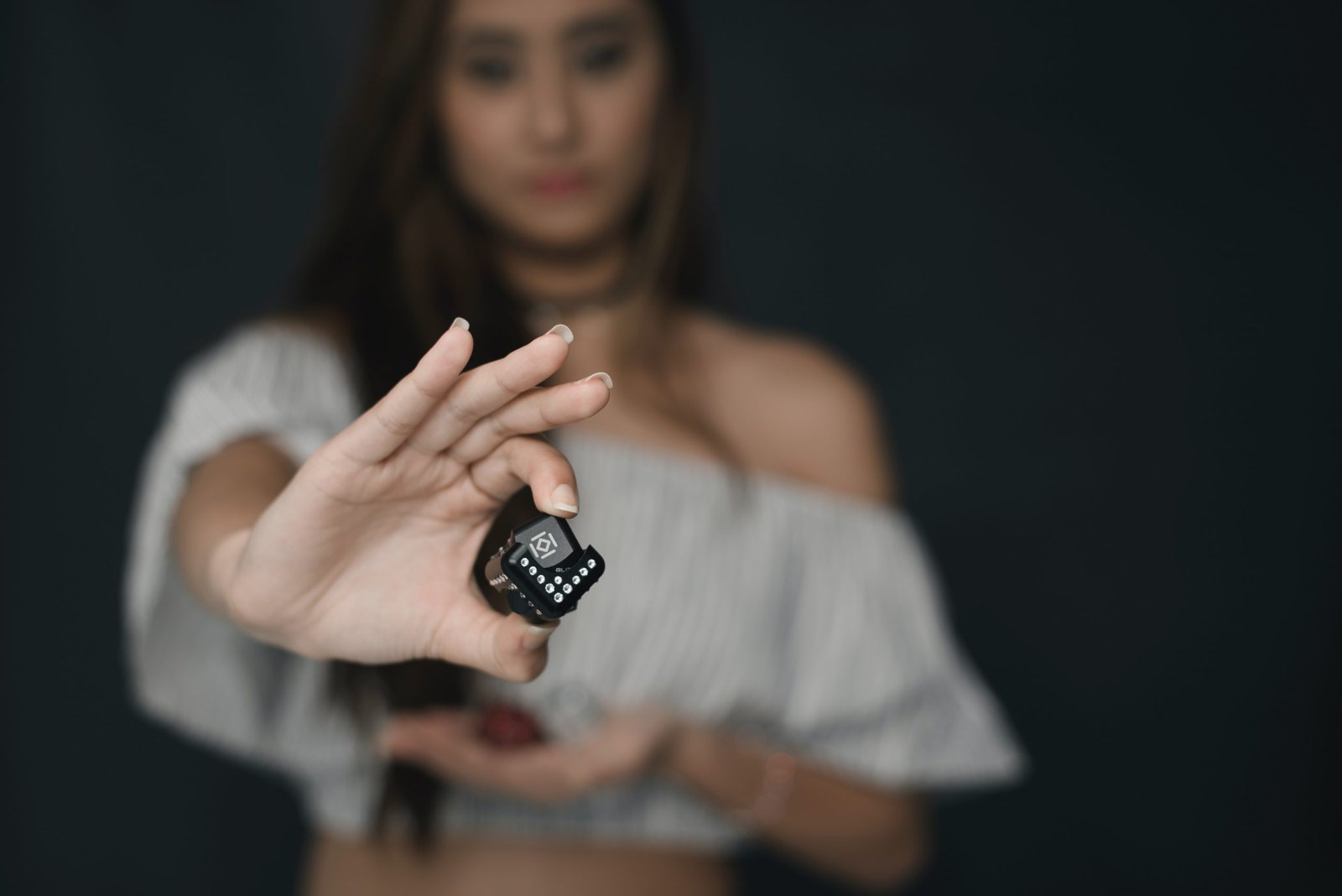 Woman wearing white off shoulder crop top holding black cube.